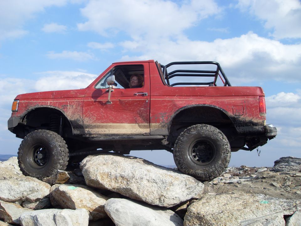 Red off-road SUV with a roll cage, mud-splattered, on large rocks