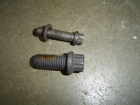 1978 Ford Bronco - Two bolts, one with rust stains, lie on a concrete surface.