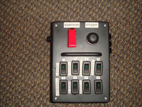 1992 Ford Bronco - Homemade black accessory switch panel photographed on carpet, with a red flip-guarded IGNITION toggle, a round ENGINE START button, and eig…