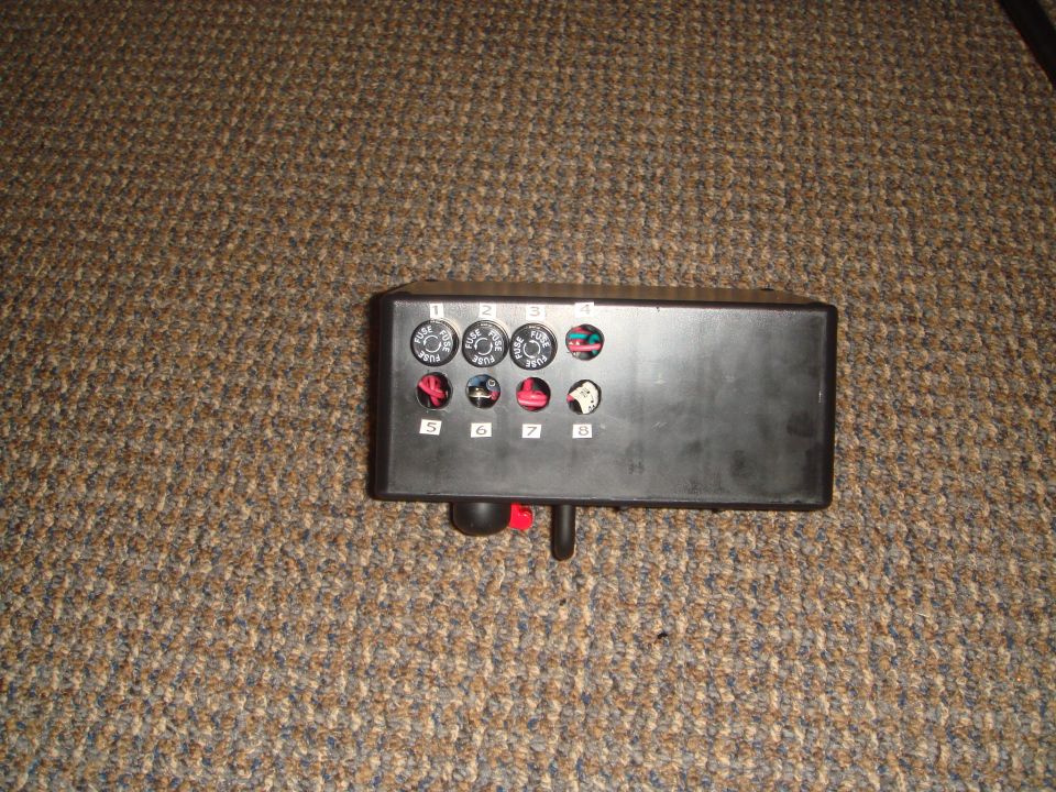 Black fuse box with 8 numbered fuse slots on brown carpet