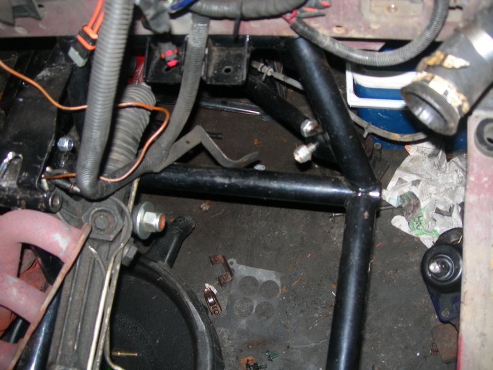 1984 Ford Bronco engine bay with roll cage, wiring, and engine parts.