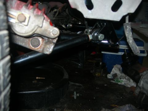 1984 Ford Bronco - A close-up view of the underside of a vehicle, showing a brake caliper, suspension components, and a black oil drain pan on the ground.