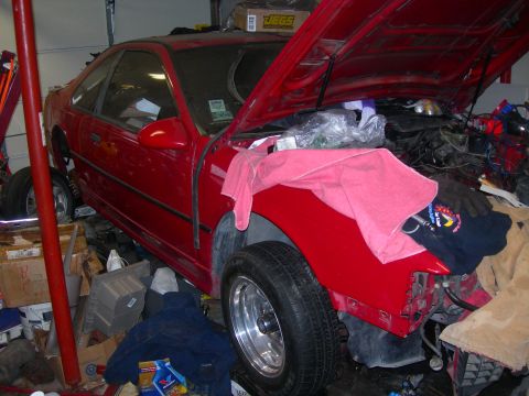 1984 Ford Bronco - A red two-door coupe is parked in a cluttered garage with its hood open, revealing the engine bay. The vehicle appears to be undergoing som…