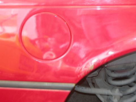 1984 Ford Bronco - A close-up view of the rear passenger side fender of a red vehicle, showing a circular gas cap door and some rust near the wheel well. The…