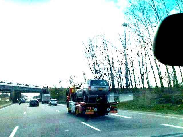Photo of a flatbed tow truck carrying a vehicle on a highway
