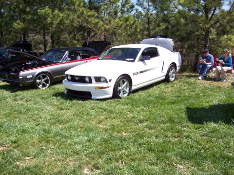 2007 Ford Mustang - A white 2007 Ford Mustang GT/CS is parked on a grassy field next to a classic gray and red car. Two people are seated in chairs in the back…