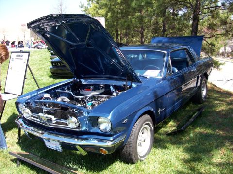2007 Ford Mustang - A blue 1965 Ford Mustang coupe is displayed with its hood open, revealing the engine bay. The car is parked on a grassy area with trees in…