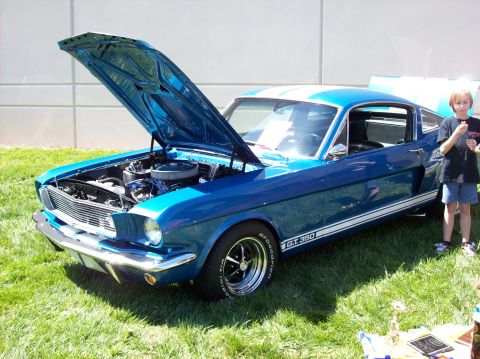 2007 Ford Mustang - A bright blue 1960s Ford Mustang GT 350 coupe is parked on a grassy lawn with its hood open, revealing the engine. A young person stands to…