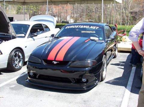 2007 Ford Mustang - A black Ford Mustang with red racing stripes on the hood and a white Mustang parked next to it with its hood open. The black Mustang has a…