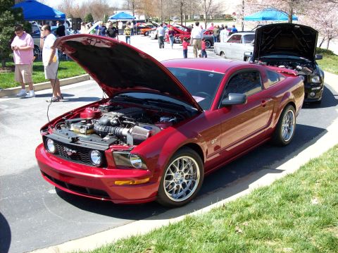 2007 Ford Mustang - A red Ford Mustang GT with its hood open is parked on a paved surface next to a grassy area. The car is a two-door coupe with custom silver…