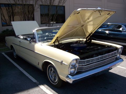 2007 Ford Mustang - A cream-colored convertible classic car with its hood open is parked in a lot. The car features chrome accents and a visible engine.