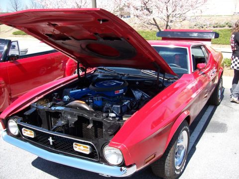 2007 Ford Mustang - A bright red classic Ford Mustang is parked outside with its hood open, revealing the engine. The car has a chrome bumper and grille, and a…