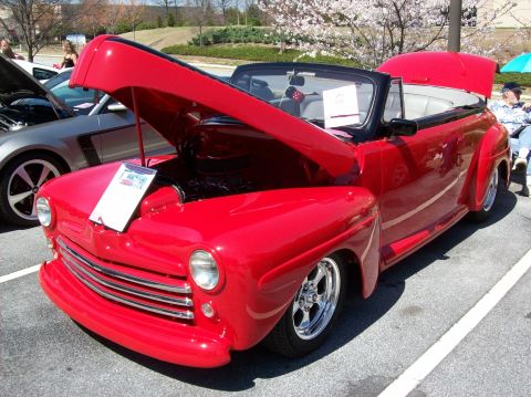 2007 Ford Mustang - A bright red classic convertible with its hood open is parked on asphalt. A silver car with its hood open is parked to the left of the red…