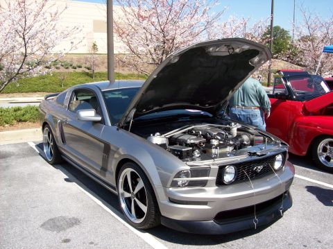 2007 Ford Mustang - A silver Ford Mustang is displayed with its hood open, parked next to a red pickup truck at an outdoor car show.