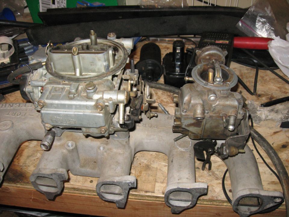 Holley 4-barrel and a smaller carburetor on an aluminum intake manifold on a workbench