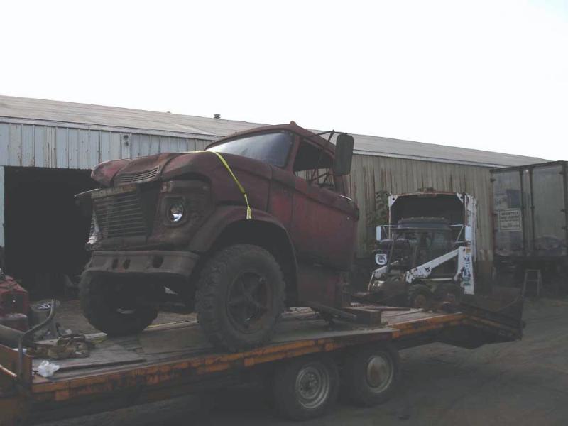 Rusty dark red vintage truck cab and chassis strapped to a flatbed equipment trailer