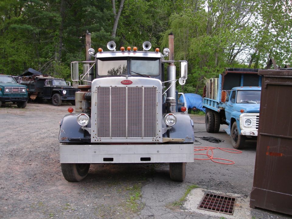 Front view of dark Peterbilt truck with chrome grille and dual stacks on gravel lot