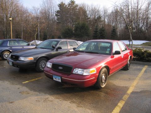 2001 Ford Crown Victoria - Three Ford Crown Victorias are parked in a lot, with the closest one being red.