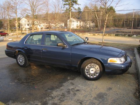 2001 Ford Crown Victoria - A dark blue Ford Crown Victoria is parked on a wet surface, with buildings and trees in the background.