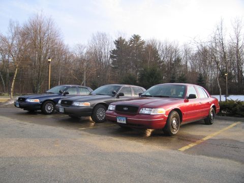 2001 Ford Crown Victoria - Three Ford Crown Victoria police cars are parked in a lot on a clear day.