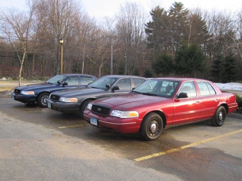 2001 Ford Crown Victoria - Three Ford Crown Victorias are parked in a lot. The red one in front has a license plate that reads 'WEB 36'.