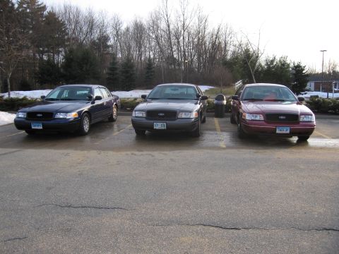 2001 Ford Crown Victoria - Three Ford Crown Victorias are parked in a lot on a cloudy day.