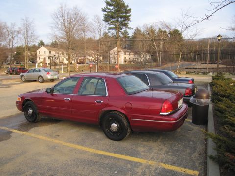2001 Ford Crown Victoria - A red sedan is parked in a lot with other vehicles visible in the background. The car is a 2001 Ford Crown Victoria.