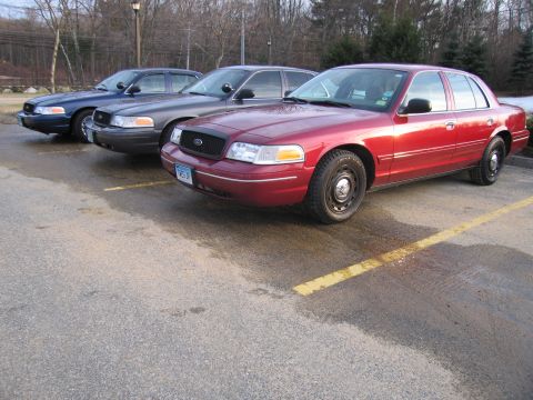 2001 Ford Crown Victoria - Three Ford Crown Victorias are parked in a lot, with the closest one being red.
