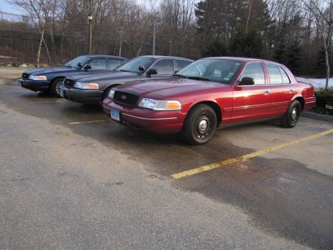 2001 Ford Crown Victoria - Three Ford Crown Victorias are parked in a lot, with the closest one being red.