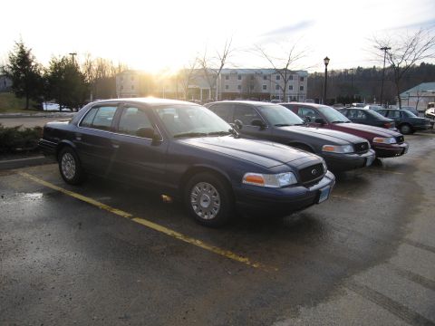 2001 Ford Crown Victoria - Several Ford Crown Victoria police cars are parked in a lot under a hazy sun.