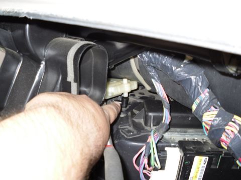 2004 Mercury Marquis - A finger points to a white plastic actuator within the vehicle's HVAC system, surrounded by ducting and a complex wiring harness.