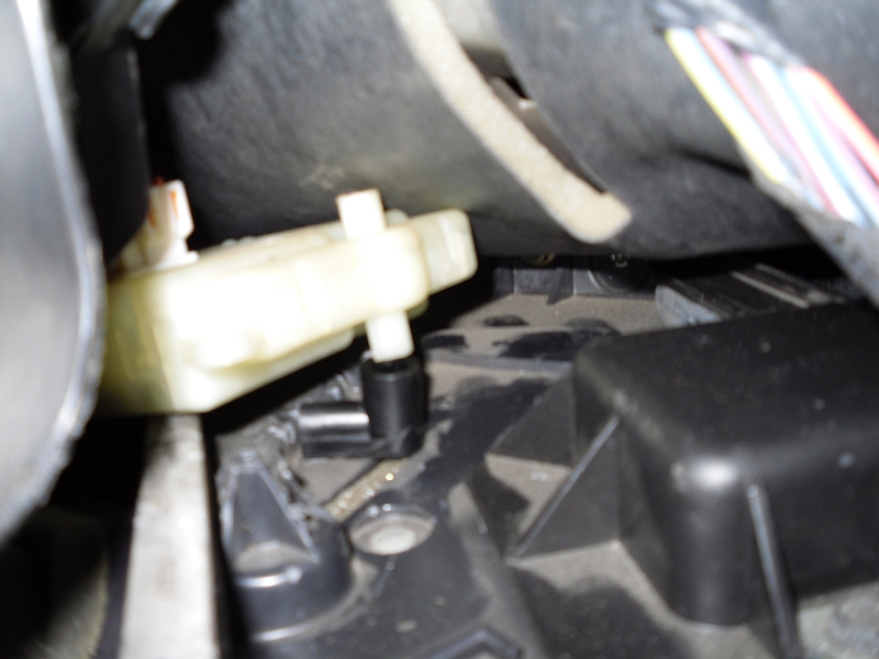 Close-up of a beige plastic lever mechanism connected to black plastic components inside a vehicle
