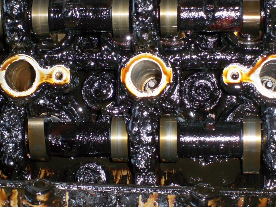 Oil-coated engine camshafts and bearing caps inside a dirty cylinder head