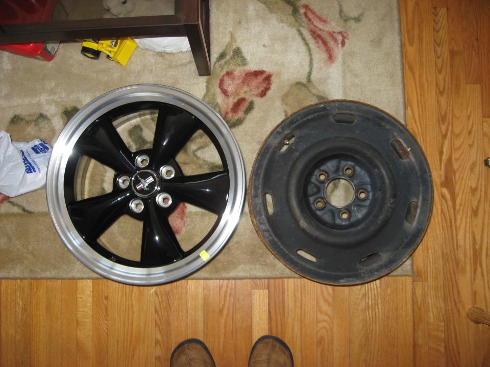 Black five-spoke alloy wheel beside a black steel wheel on a floor
