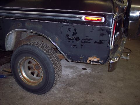1979 Ford Bronco - The rear quarter panel of a black 1979 Ford Bronco displays significant rust damage and a functioning side marker light.