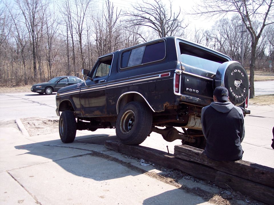 Black Ford Bronco with a spare tire on the back, parked on a curb.