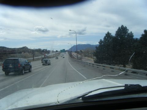 1979 Ford Bronco - A dark blue SUV is driving on a highway under a cloudy sky. The photo is taken from inside another vehicle, looking through the windshield.