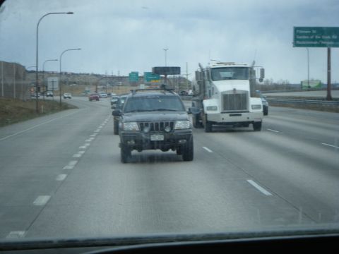 1979 Ford Bronco - A dark-colored Jeep Grand Cherokee is driving on a highway behind a white semi-truck. The Jeep is in the foreground and the semi-truck is i…