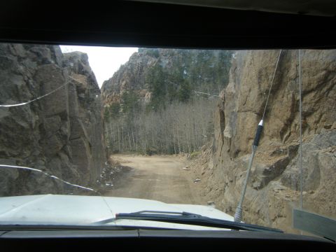 1979 Ford Bronco - View from inside a vehicle driving on a dirt road through a narrow canyon with steep rock walls. The windshield shows cracks and a radio an…