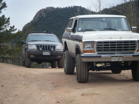 1979 Ford Bronco - A white 1979 Ford Bronco is parked on a dirt road in front of a mountain range, with a dark SUV to its left.