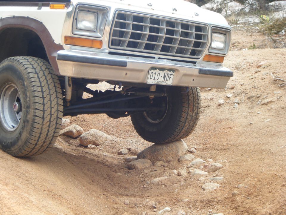 White 1979 Ford Bronco front passenger side tire on a rock, Colorado license plate visible.