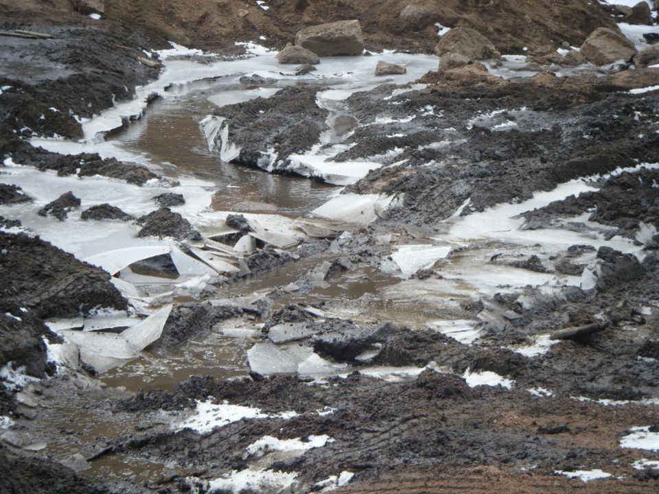 Muddy and icy landscape with broken ice chunks.
