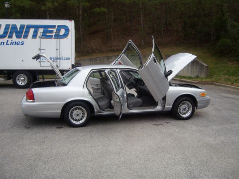 1993 Ford Crown Victoria - A silver 1993 Ford Crown Victoria with lambo doors and the hood open is parked next to a white United Van Lines truck. The trunk of the Cro…