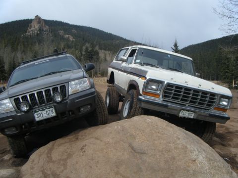 1979 Ford Bronco - A gray Jeep Grand Cherokee and a white Ford Bronco are parked on a large rock formation in a wooded, mountainous area.