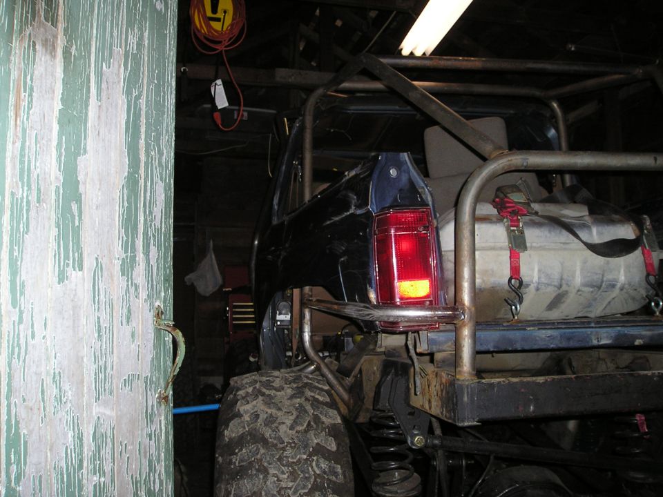 Rear driver's side of a dark blue modified SUV with roll cage and auxiliary fuel tank.