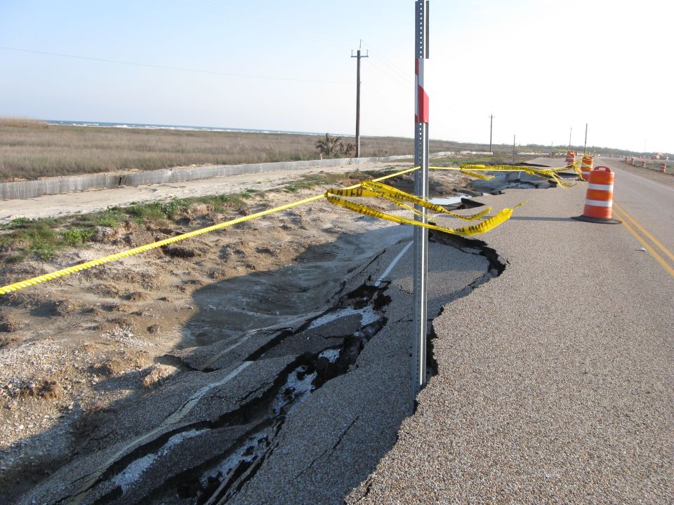 Storm-damaged coastal road with washed-out shoulder and caution tape