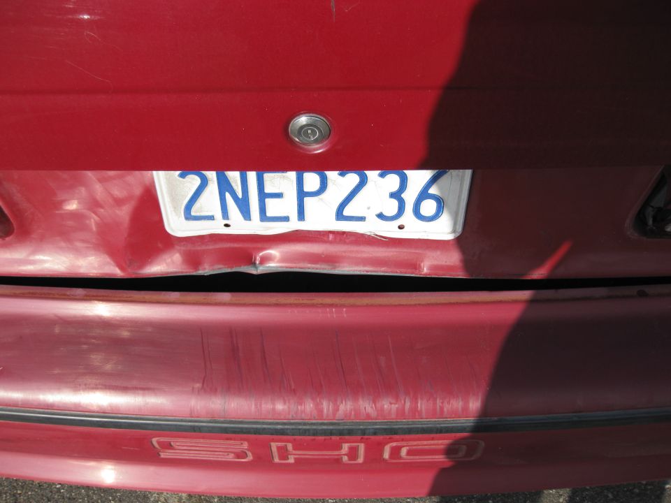 Rear of a red 1989 Ford Taurus with a dented trunk and bumper, license plate 2NEP236.