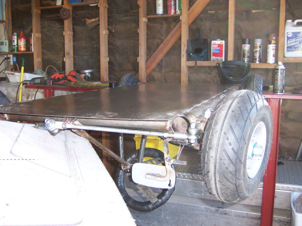 Photo of a flat-deck go-kart frame with rear wheel in a garage