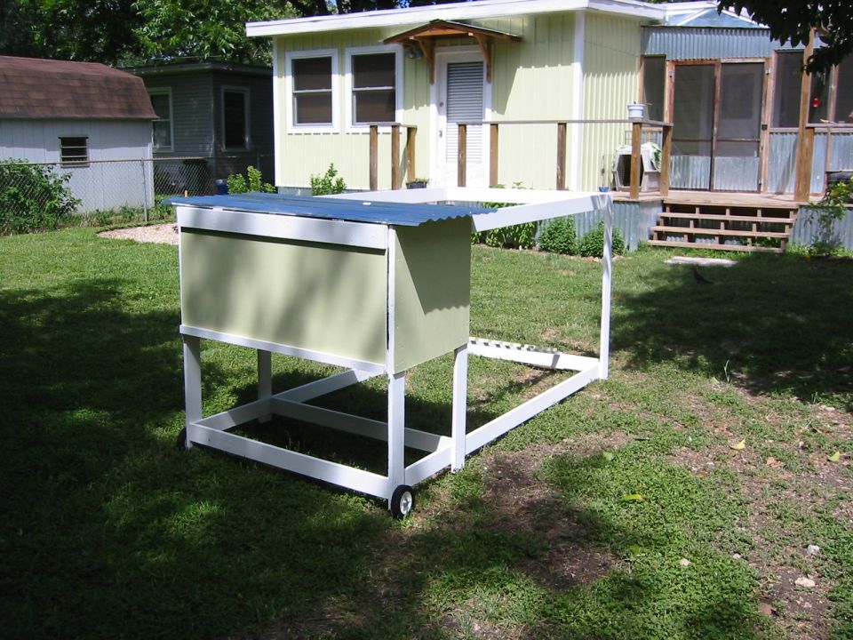 A chicken coop with a corrugated metal roof on a grassy lawn.
