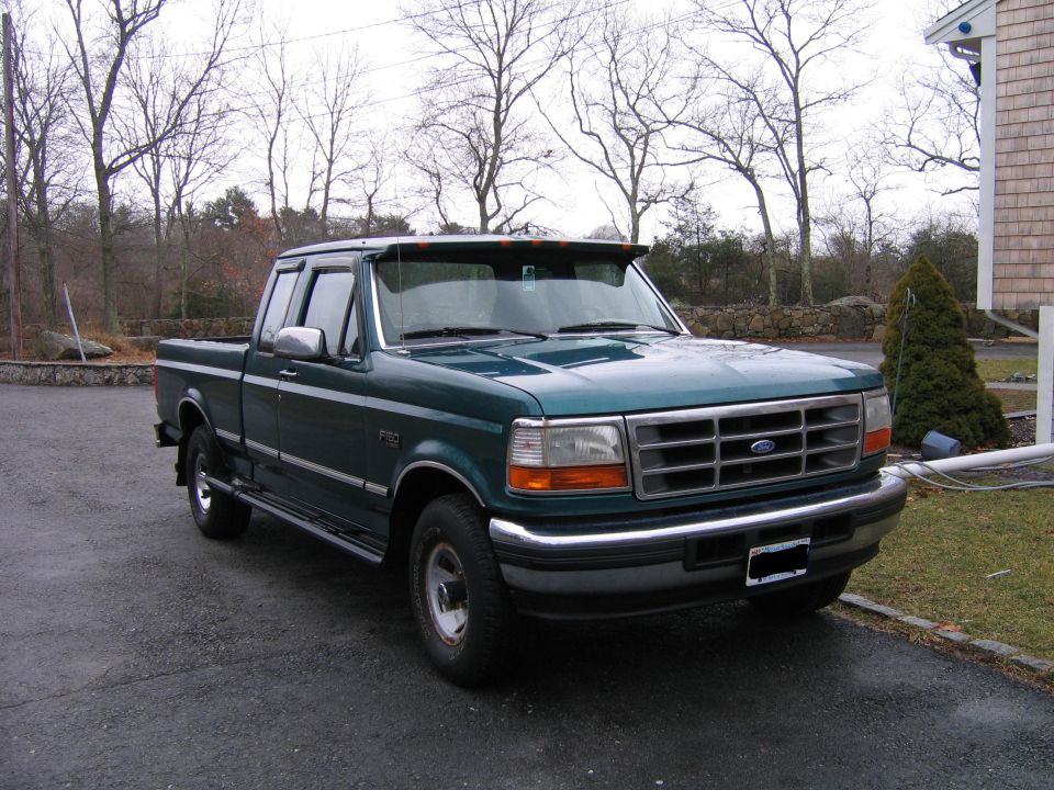 1996 Ford F-150 pickup truck, dark green, parked on asphalt driveway.